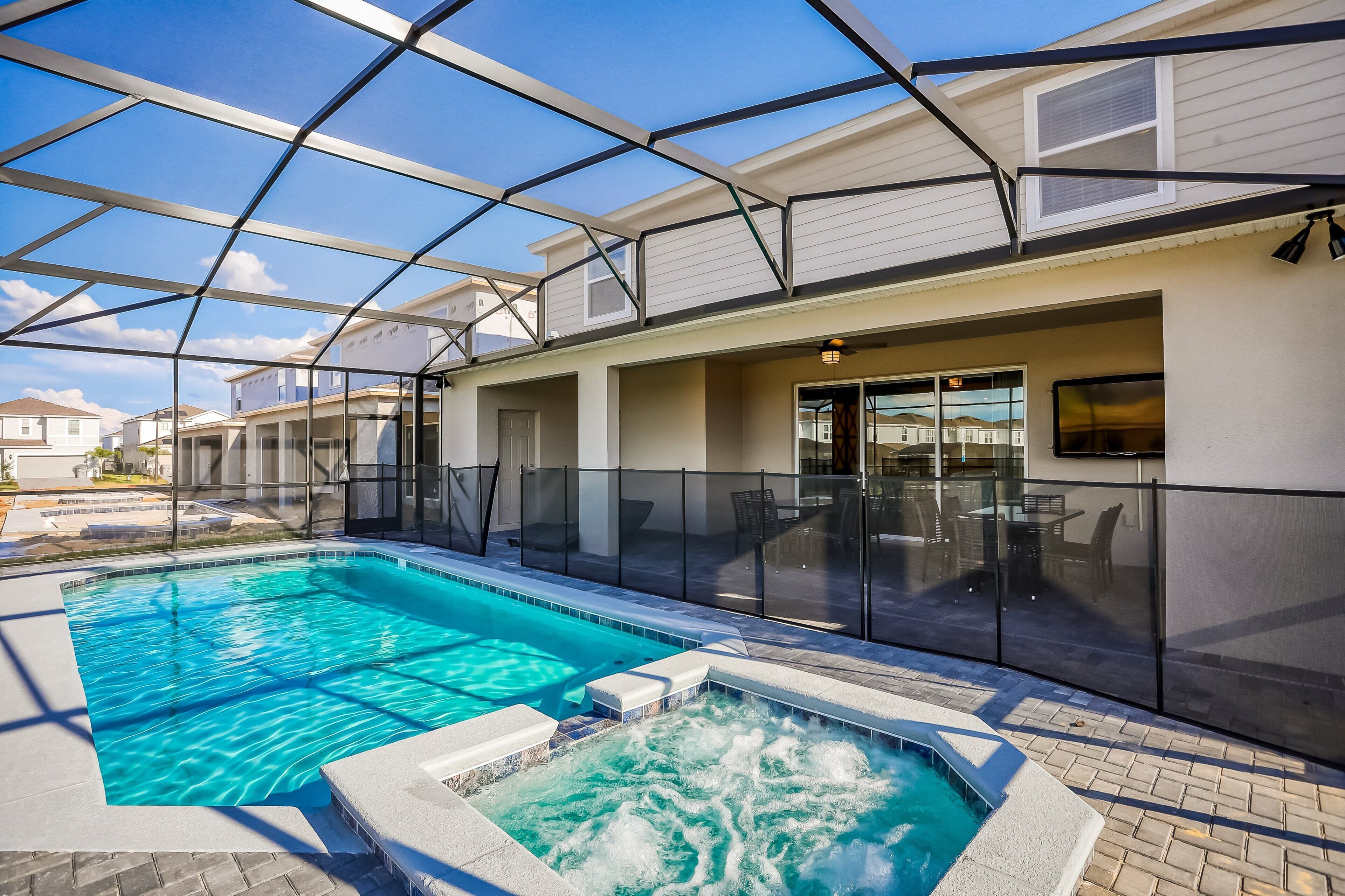 A swimming pool with a hot tub, a covered patio area, and a view of neighboring houses.