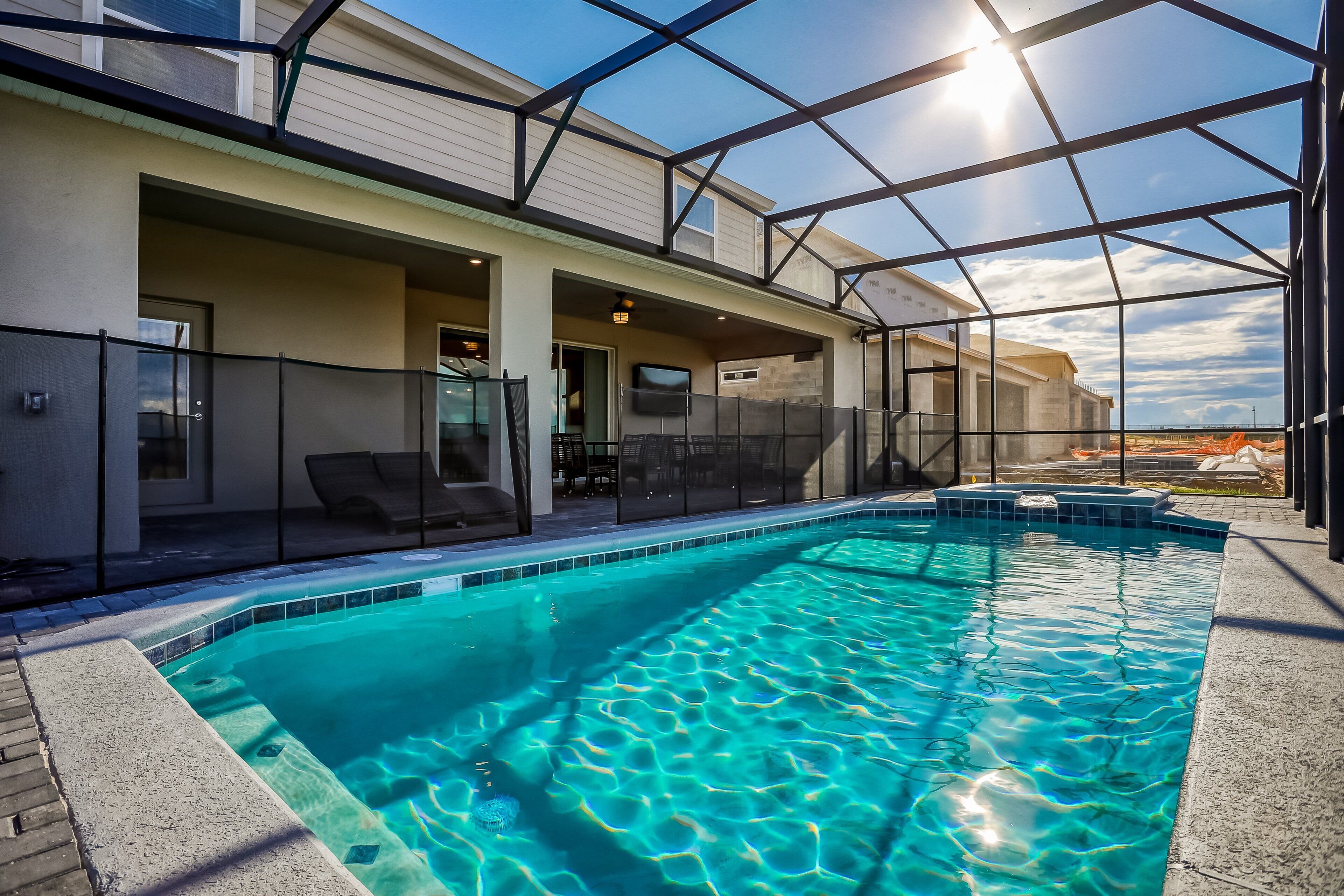 A swimming pool with a glass enclosure, a covered patio with chairs, and a view of a building under construction.