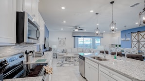 A modern kitchen with a central island, built-in appliances, and a dining area with a sofa and chairs. - New Home With Private Pool/spa & Resort Waterpark/arcade Access (Davenport)