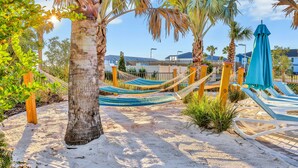 A sandy beach area with hammocks, lounge chairs, and a blue umbrella. - New Home With Private Pool/spa & Resort Waterpark/arcade Access (Davenport)