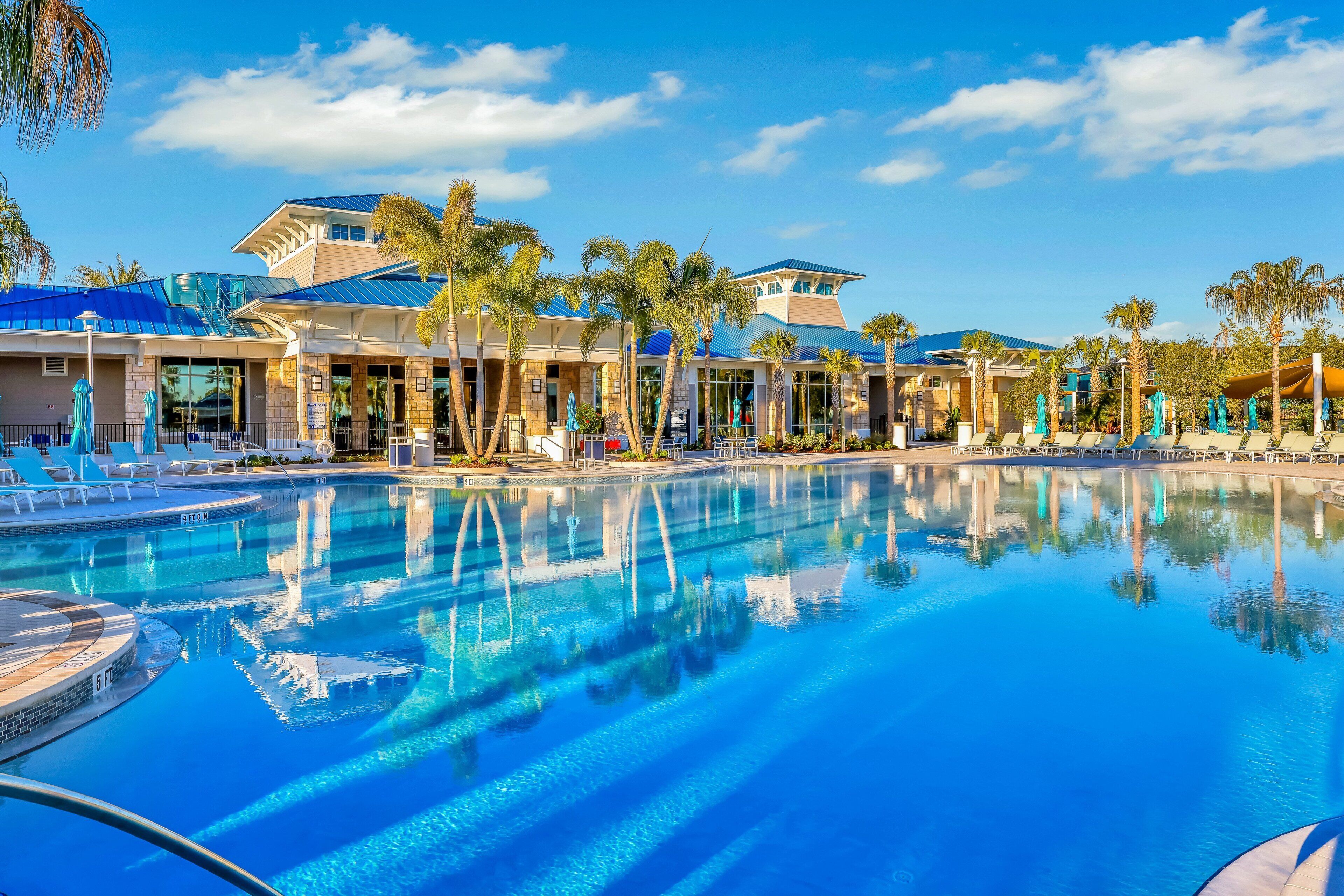 A pool with clear water, surrounded by palm trees and lounge chairs, with a building in the background.