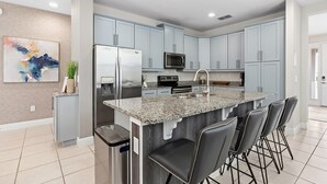 A modern kitchen with granite countertops, stainless steel appliances, and light blue cabinets. - Dog-friendly Getaway With Private Pool + Spa, Putting Green, Patio, & Game Room (Kissimmee)
