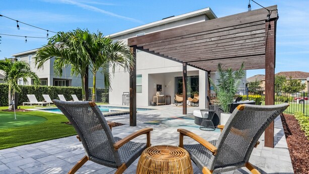 A patio area with two wicker chairs, a woven stool, and a pergola. - Dog-friendly Getaway With Private Pool + Spa, Putting Green, Patio, & Game Room (Kissimmee)