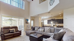 A spacious living room with a sectional sofa, ottoman, and a view of the kitchen. - Dog-friendly Home With Private Pool, High-speed Wifi, Central AC, & Washer/dryer (Kissimmee)
