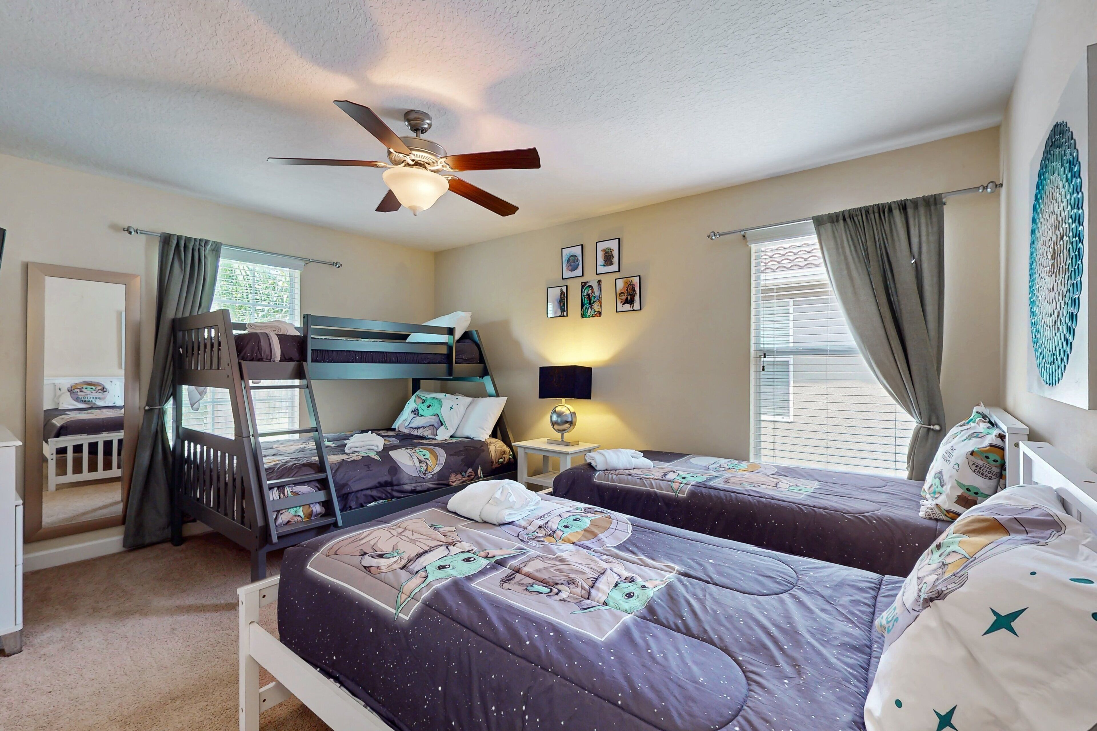 A bedroom with bunk beds, a ceiling fan, a bedside table with a lamp, and a window with curtains.