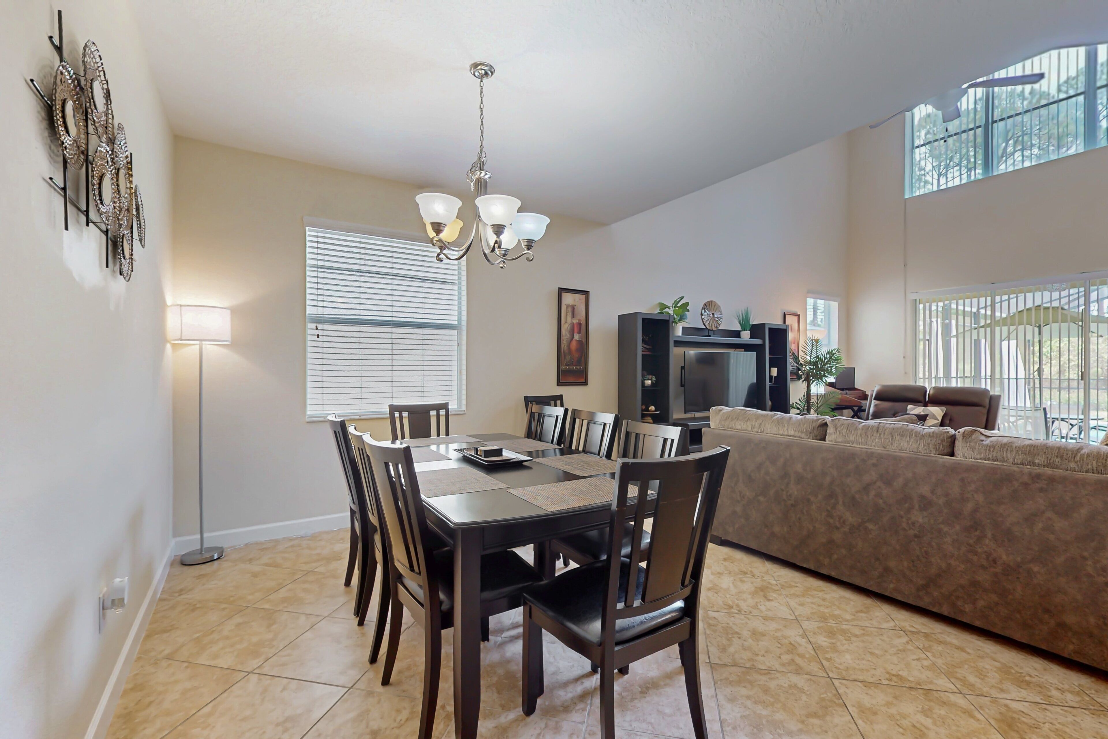 A dining area with a table and chairs, a chandelier, a sofa, and a television.