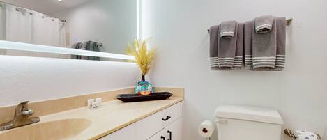 A bathroom with a sink, mirror, toilet, and towels.
