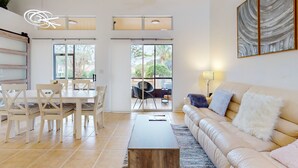 A modern living room with a sofa, coffee table, dining table with chairs, and artwork on the wall. - Ideally Located Modern Townhome With Open Layout & Pool - Snowbird-friendly (Kissimmee)