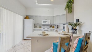A modern kitchen with white cabinets, a microwave, and a dining area with wooden chairs and a central island. - Dog-friendly Condo With Gym, Wifi, Balcony - Close to Theme Parks (Orlando)