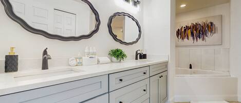 Un bagno con un mobile lavabo bianco, due grandi specchi, un lavandino, un rubinetto, una pianta e una vasca da bagno.