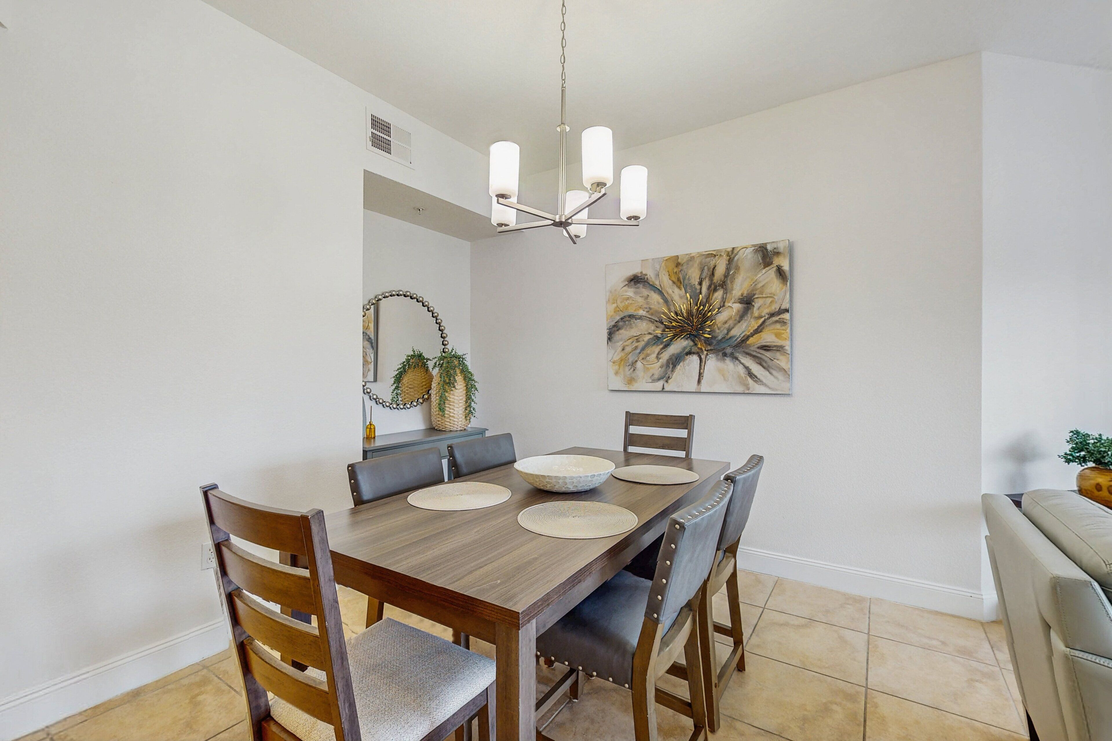 Un comedor con una mesa de madera, sillas, una araña y un cuadro en la pared.