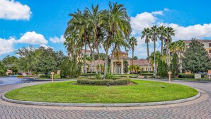 A landscaped area with palm trees, a circular driveway, and a building with a yellow facade. - Dog-friendly Condo With Gym, Wifi, Balcony - Close to Theme Parks (Orlando)