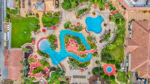Ein Luftbild eines Resorts mit mehreren Schwimmbecken, Liegestühlen und üppiger Bepflanzung.