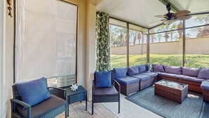 Ein überdachter Patio-Bereich mit Korbmöbeln, einem Deckenventilator und Blick auf eine grüne Landschaft.