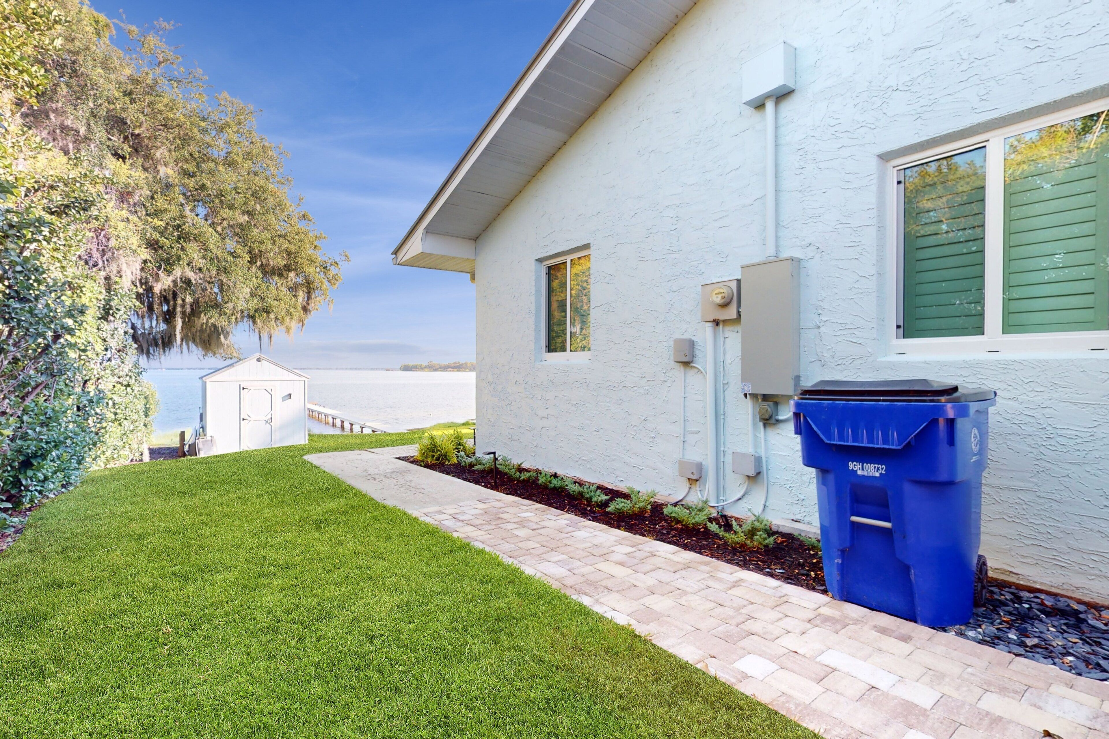 A house with a white exterior, a brick pathway, and a blue trash bin.
