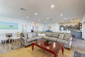 Una sala de estar con un sofá modular, una mesa de centro y un comedor con una mesa blanca y sillas.