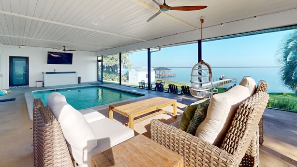 Area piscina interna moderna con vista sul mare, mobili in vimini e ventilatore a soffitto.