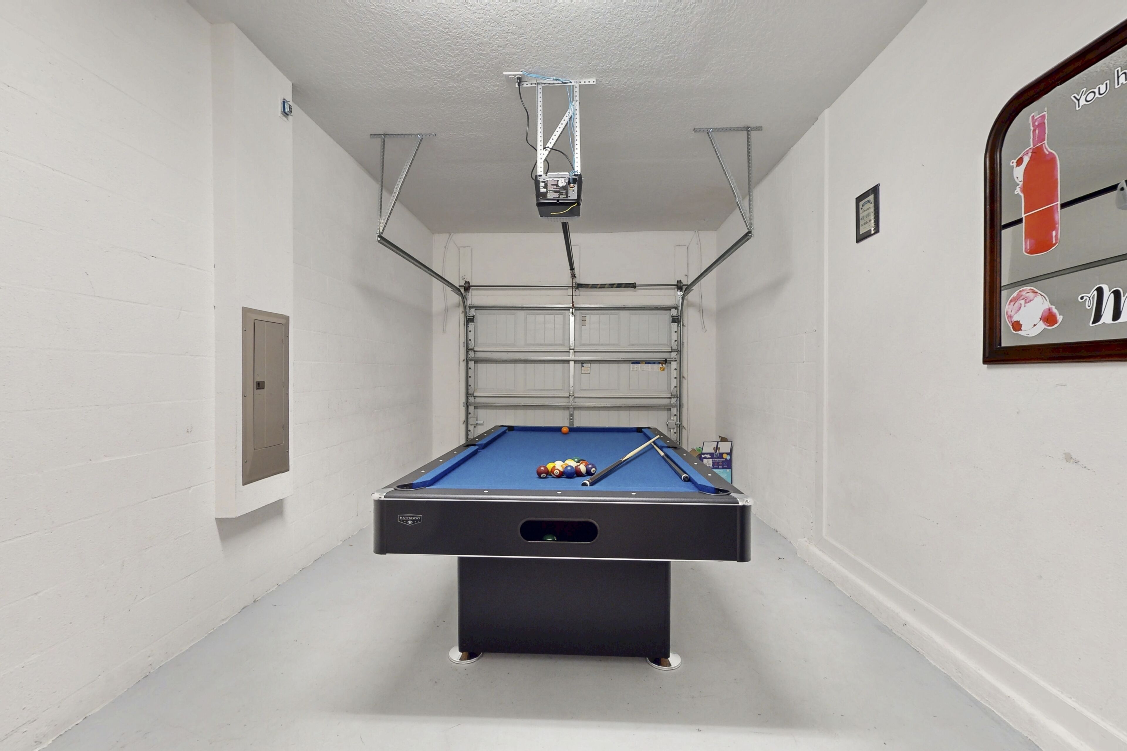 A pool table in a room with white walls and a ceiling-mounted projector.