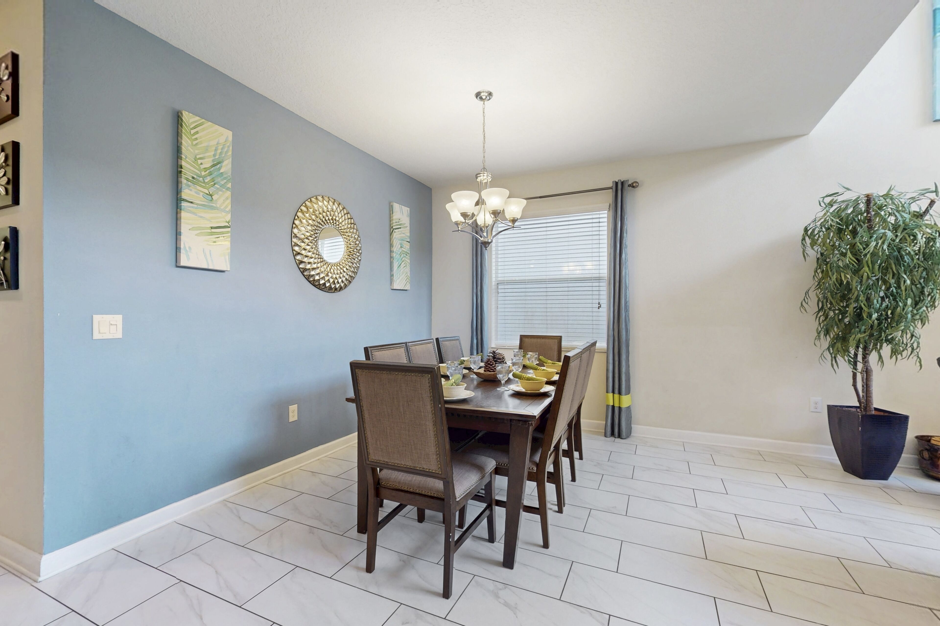 A dining area with a table set for four, surrounded by chairs, a chandelier, and a potted plant.