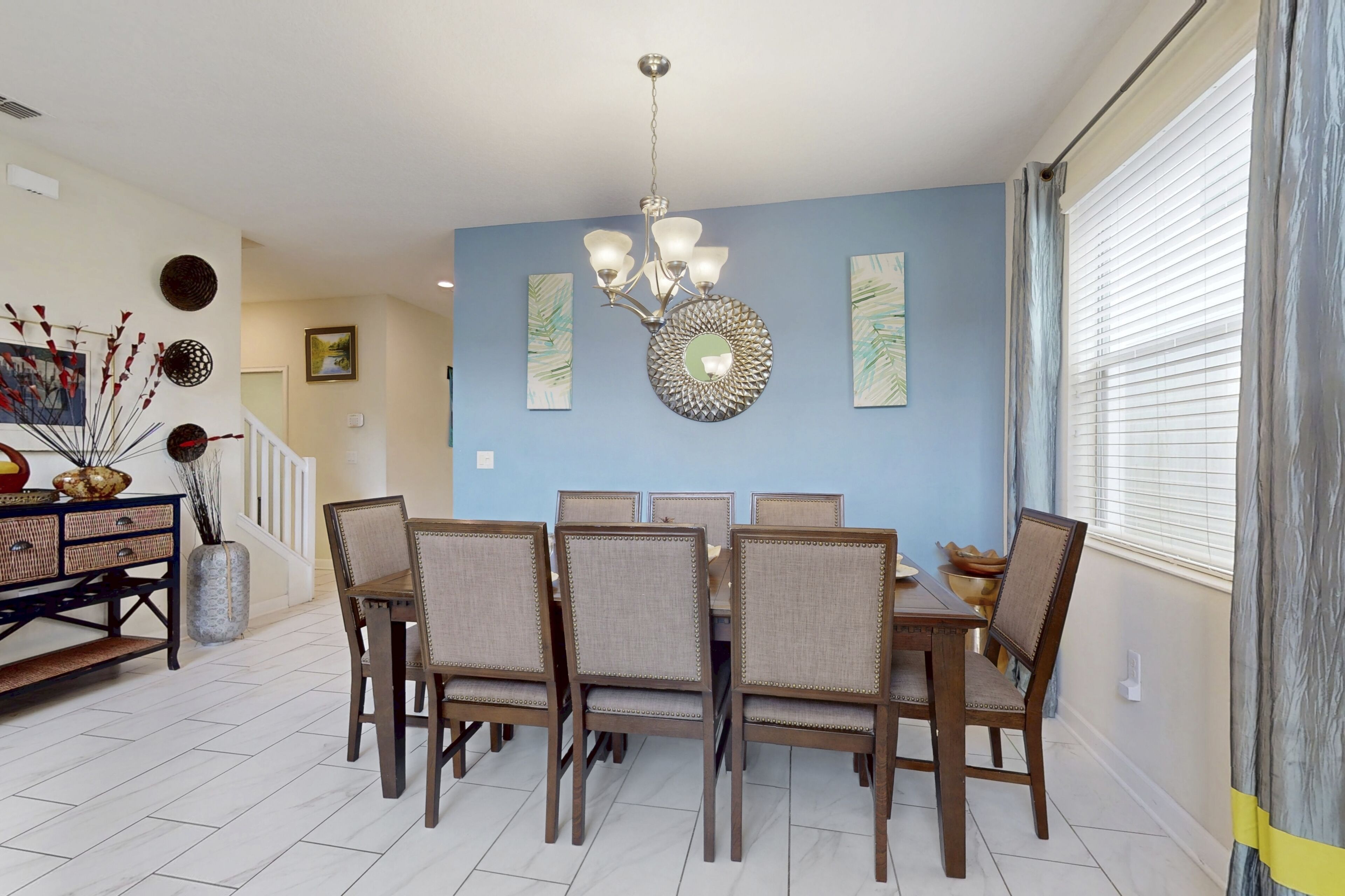 Un coin repas avec un mur bleu, un lustre et une table à manger entourée de six chaises.
