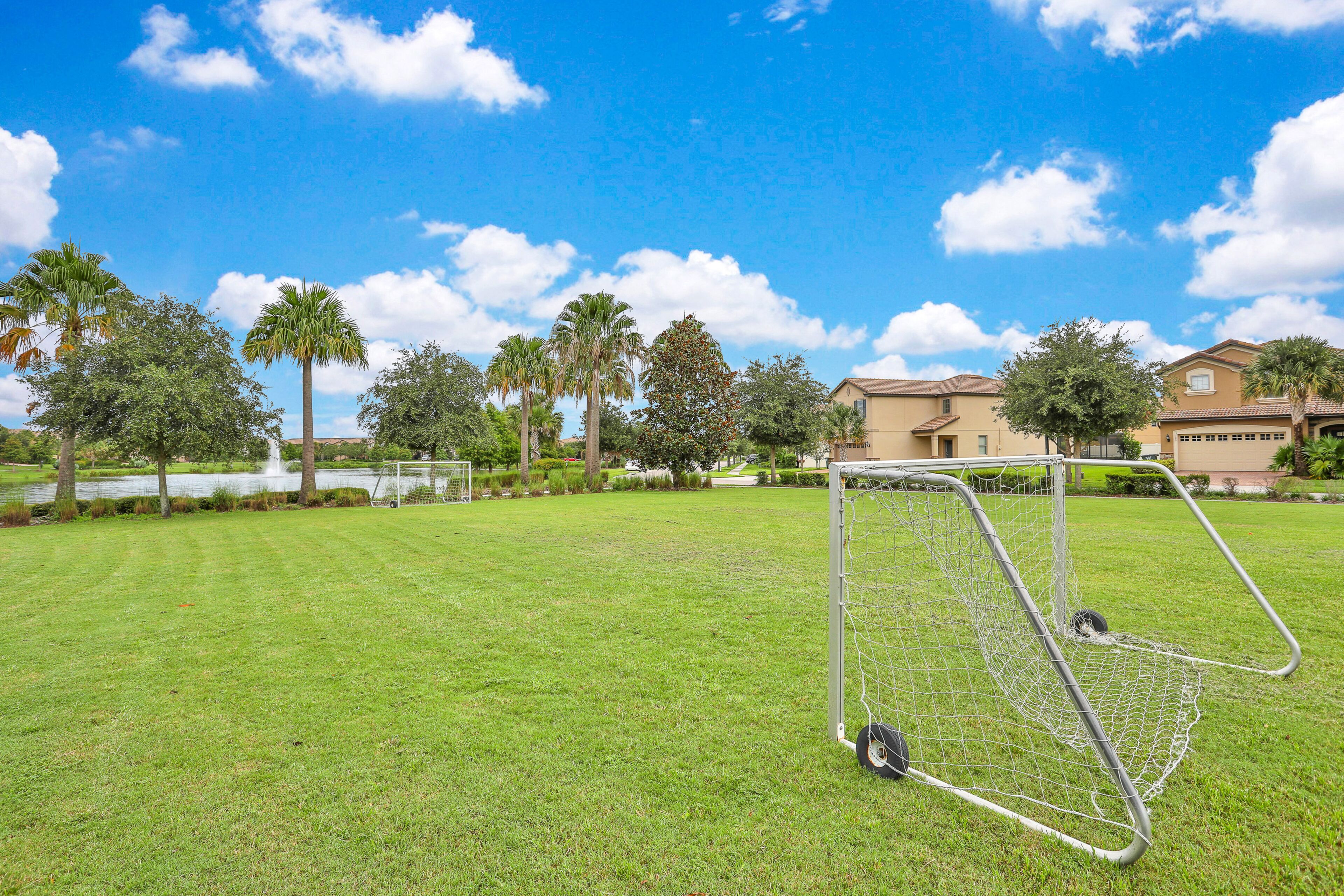 Un arco de fútbol en un campo de césped bien cuidado, con palmeras y casas al fondo.