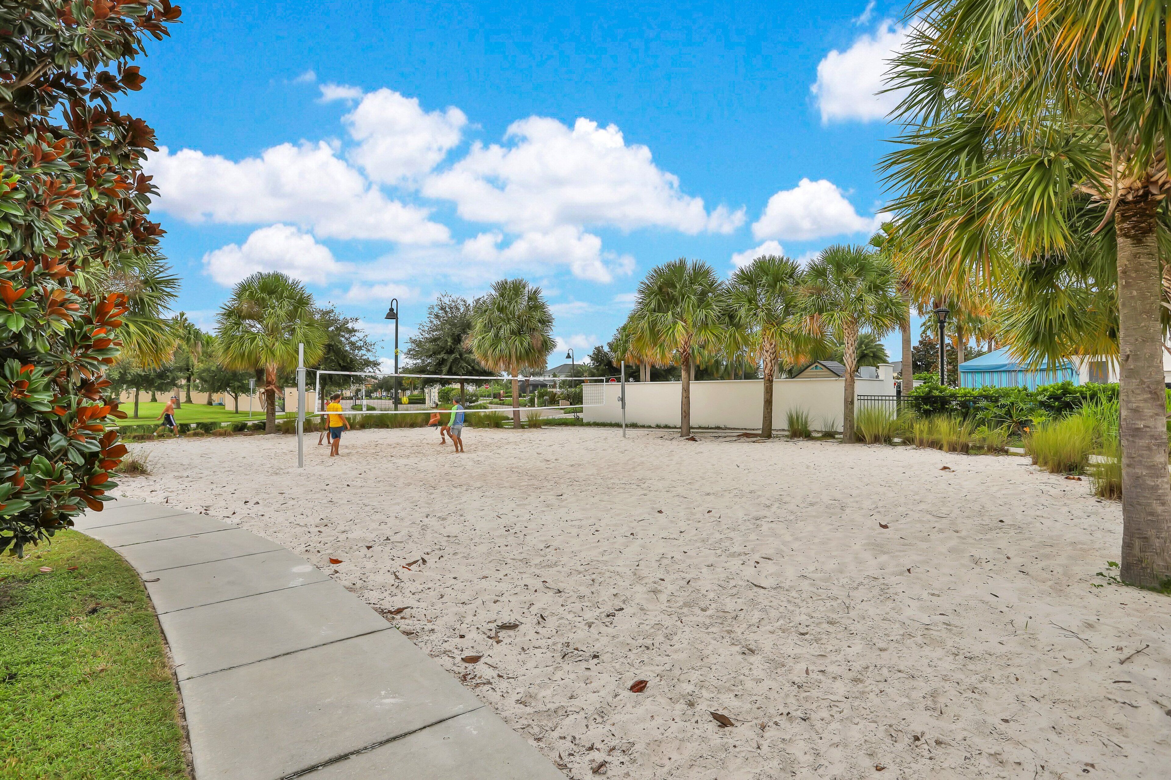 A sandy volleyball court with palm trees and a clear sky.