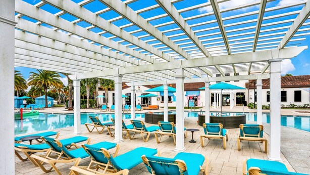 A poolside area with lounge chairs, a covered section with a view of the pool, and a building in the background. - Spacious Home w/ Private Pool, Wifi, Central AC, Private Washer/dryer (Kissimmee)