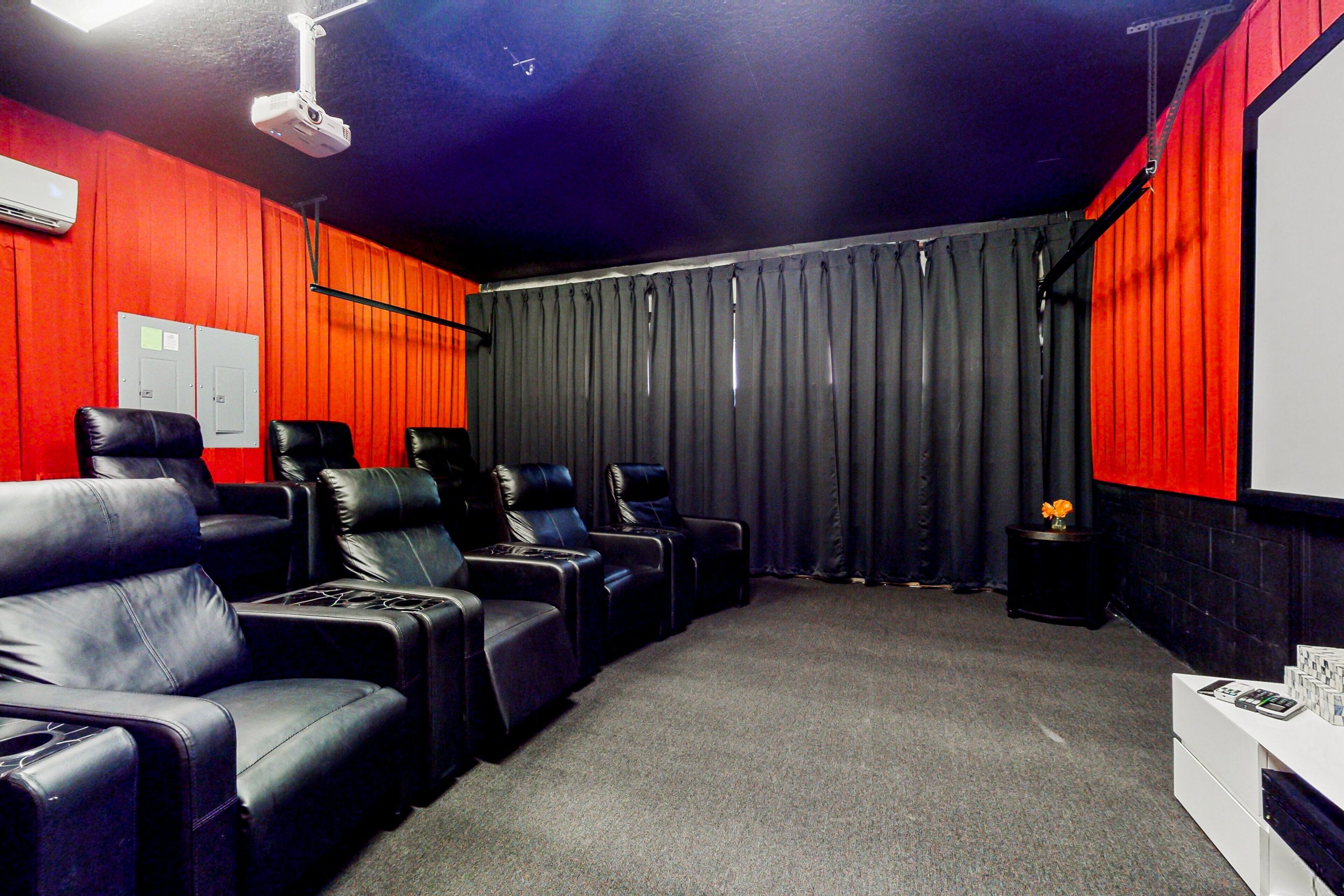 A room with a red wall, black leather recliners, a projector, and a white console with magazines.