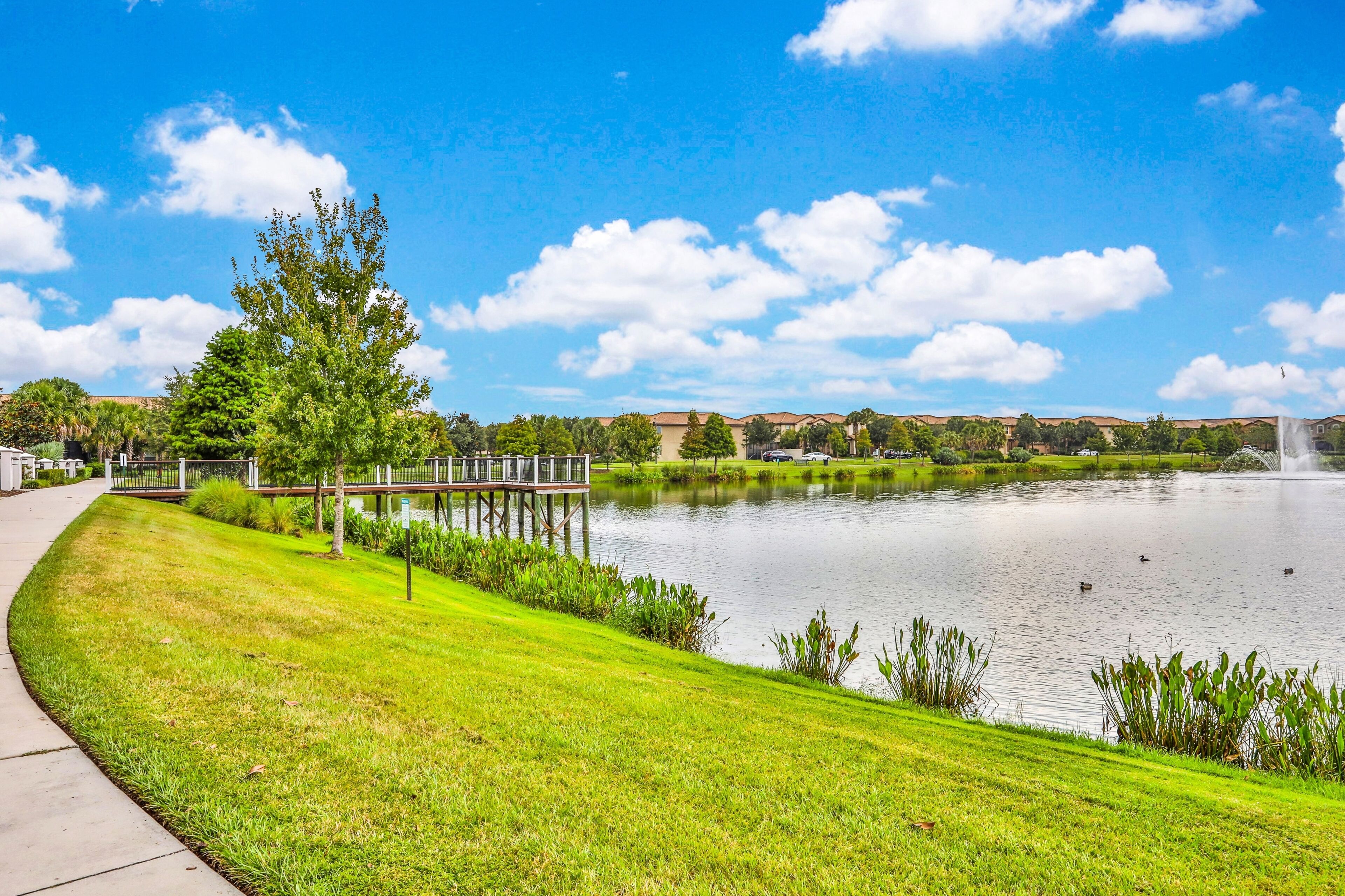 A serene lakeside view with a wooden dock, grassy banks, and a clear blue sky.