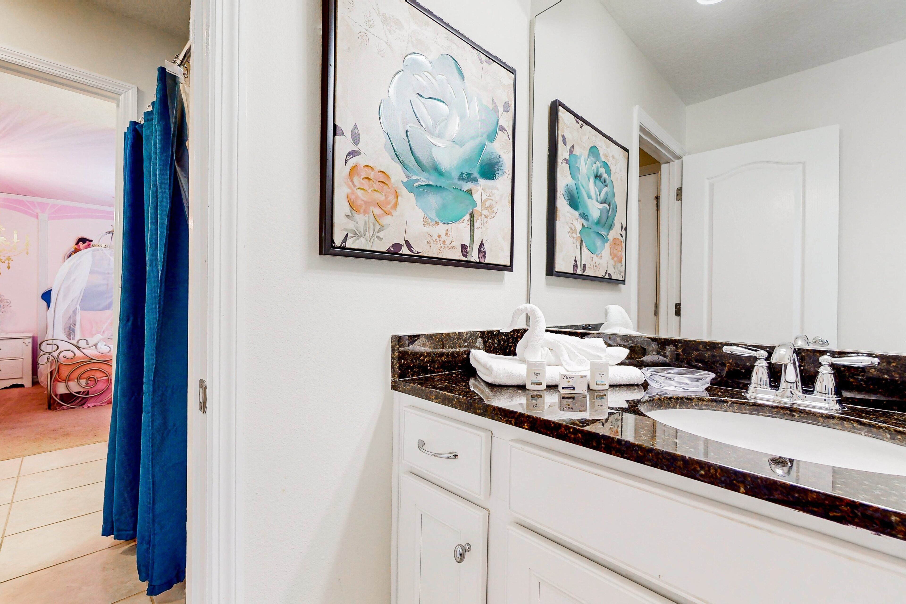 A bathroom with a white vanity, a sink with a marble countertop, and two framed floral paintings on the wall.