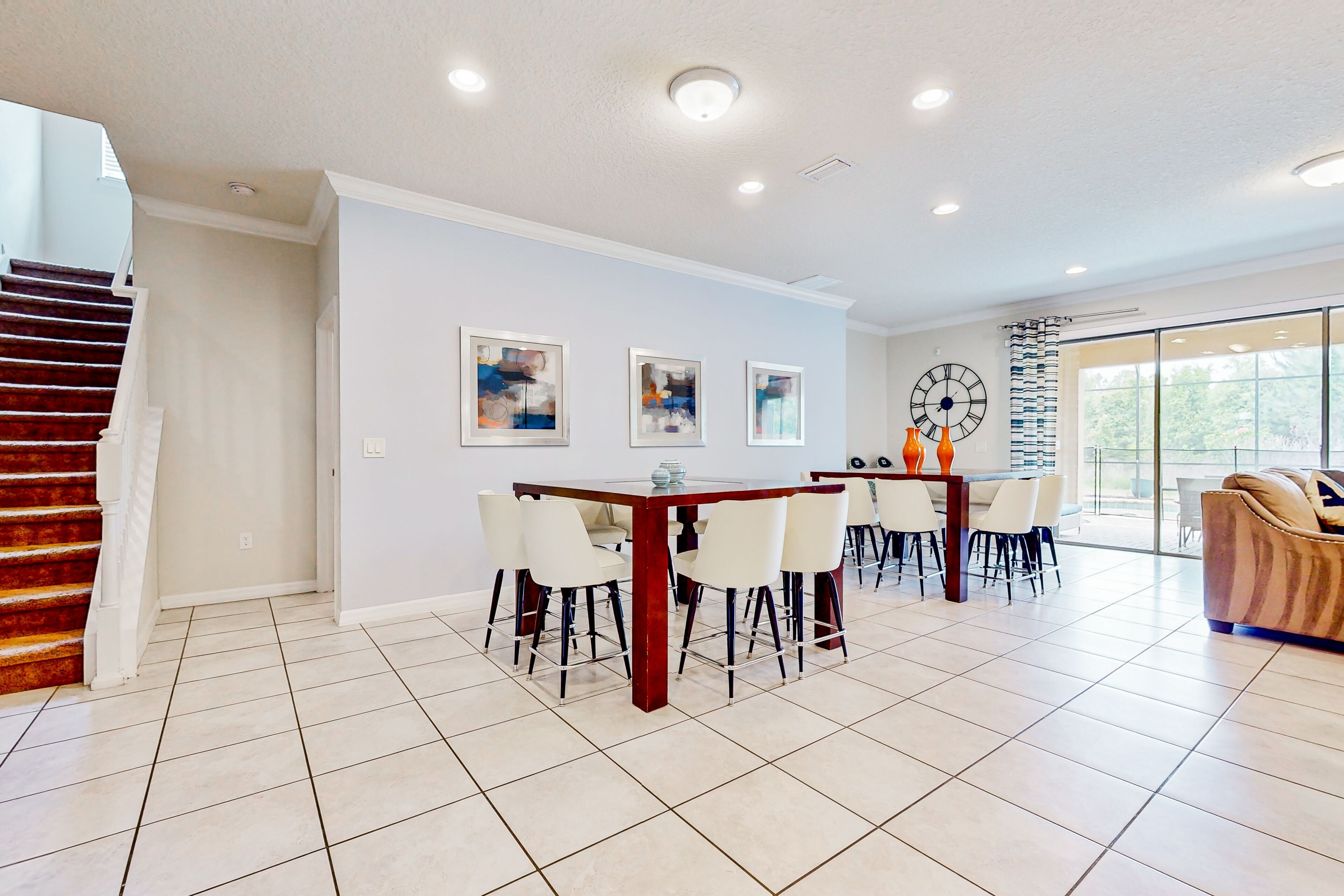 A spacious dining area with a wooden table and chairs, a staircase, and a large window with a view.