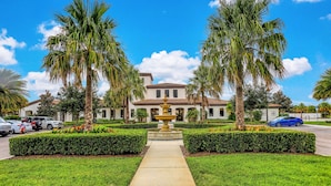 A well-maintained garden with a central fountain, palm trees, and a pathway leading to a building with a tiled roof. - Spacious Home w/ Private Pool, Wifi, Central AC, Private Washer/dryer (Kissimmee)