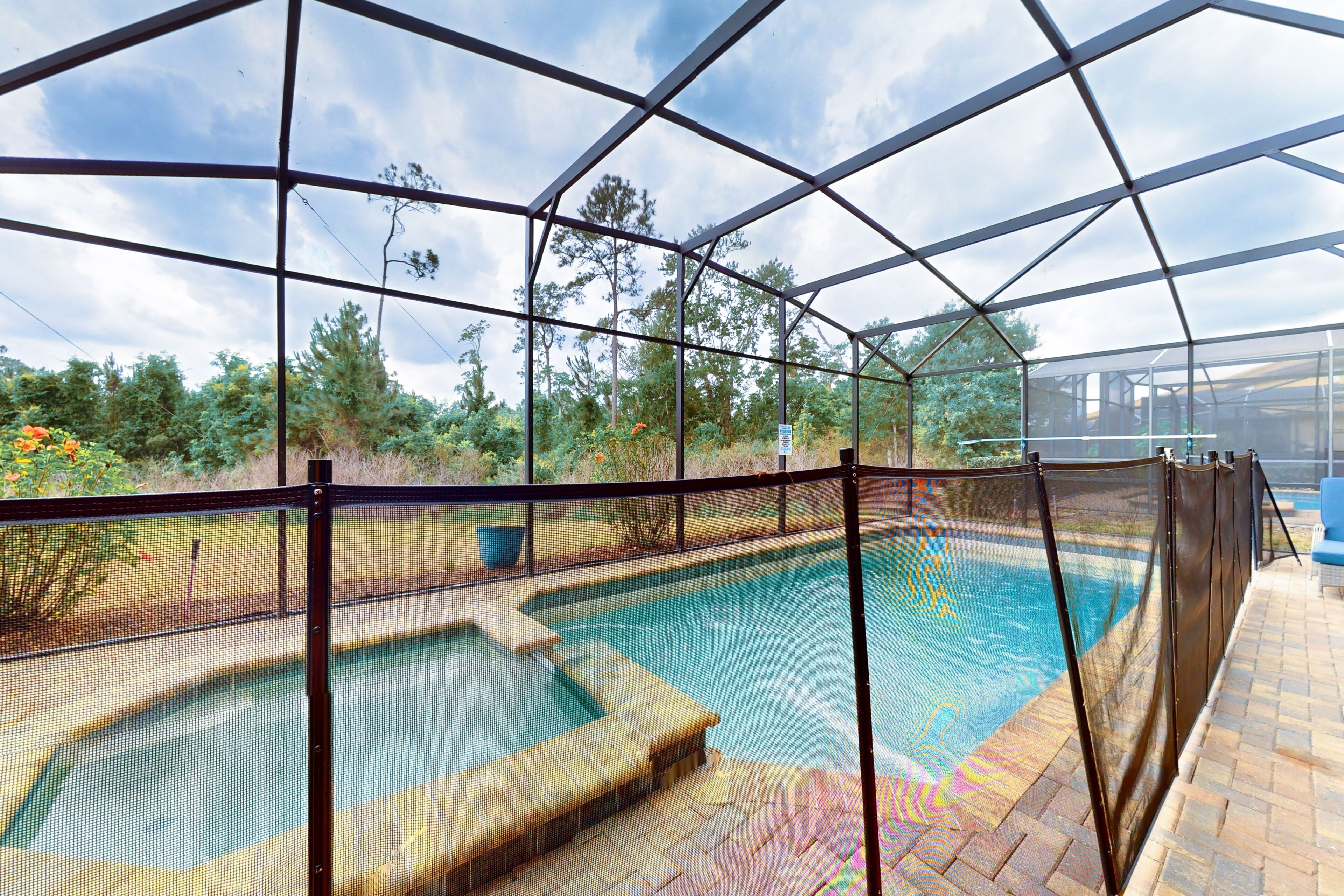 A pool area with a glass enclosure, a hot tub, and a patio with a blue chair.