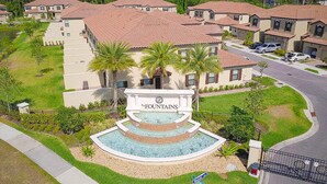A residential area with a central fountain, houses with red-tiled roofs, and a gated entrance. - Charming Dog-friendly Home With Pool, hot Tub, Fitness Center, Patio, & Kitchen (Davenport)