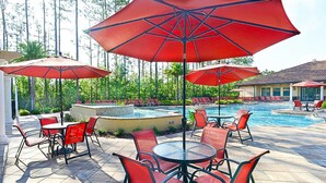 A poolside area with red umbrellas, red chairs, and a tiled floor. - Charming Dog-friendly Home With Pool, hot Tub, Fitness Center, Patio, & Kitchen (Davenport)