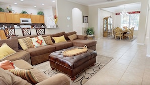Ein geräumiges Wohnzimmer mit braunem Ledersofa, dazu passendem Hocker und einem Essbereich mit Holztisch und Stühlen.