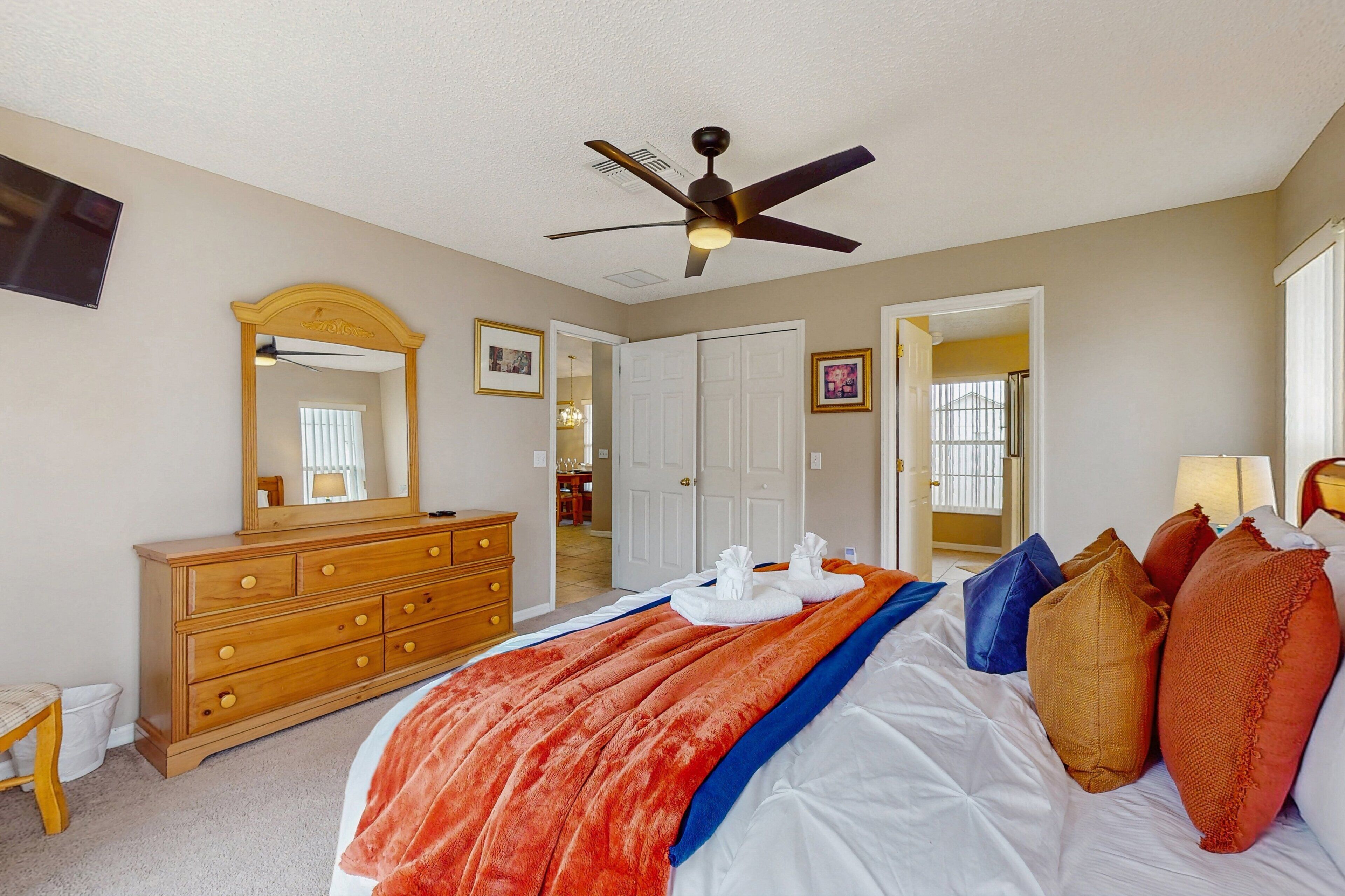 A bedroom with a bed, a dresser, a ceiling fan, and a large mirror.