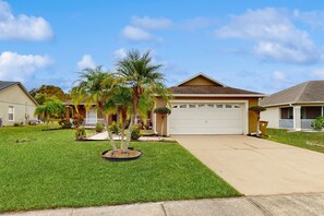 A residential house with a garage, a well-maintained lawn, and a palm tree. - Inviting Pool Home With Tranquil Pond View Near Theme Parks & Attractions (Kissimmee)