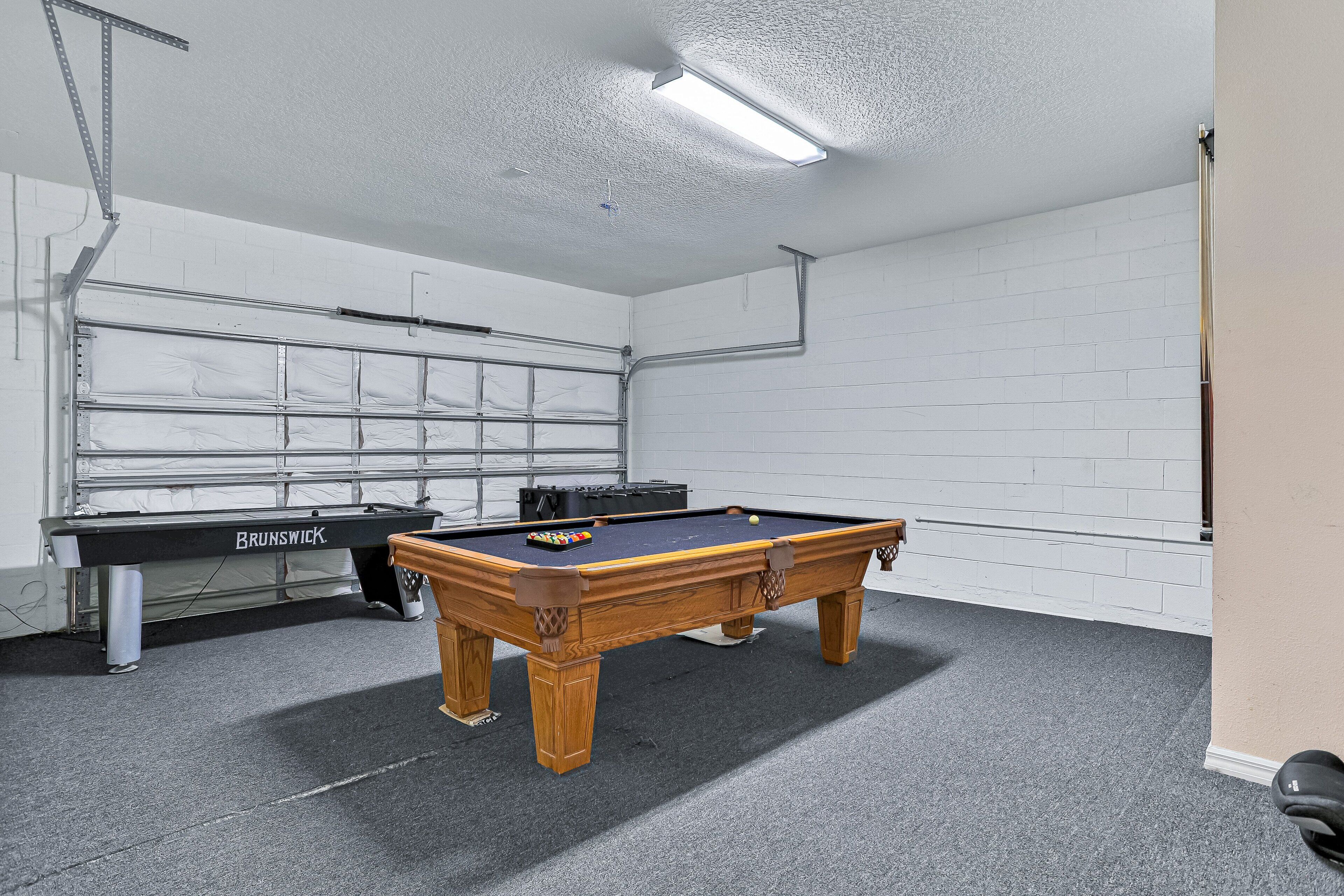 Et biljardbord i et rum med hvide murstensvægge, en loftslampe og en garageport.