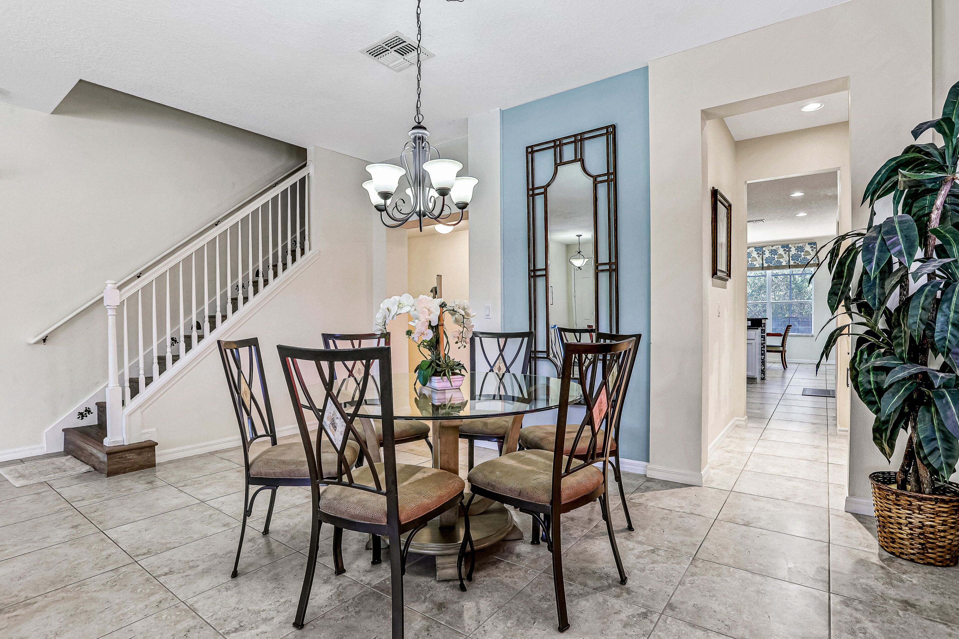 A dining area with a round table, four chairs, a chandelier, and a staircase.