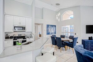 A modern kitchen with white cabinetry, a microwave, and a stove. There is a dining area with blue chairs and a table. - Beautiful Home With Private Pool, Screened Lanai, Wifi, Private W/d, and AC (Kissimmee)