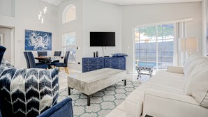 A spacious living room with a flat-screen TV, a dining area with chairs, a sofa, and a patterned rug. - Beautiful Home With Private Pool, Screened Lanai, Wifi, Private W/d, and AC (Kissimmee)