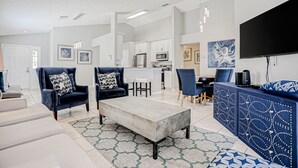 A modern living room with a sofa, coffee table, and blue armchairs. There is a kitchen area with a microwave and a dining table with chairs. - Beautiful Home With Private Pool, Screened Lanai, Wifi, Private W/d, and AC (Kissimmee)