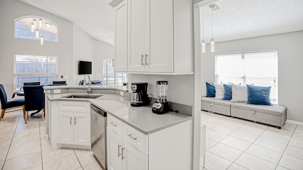 A modern kitchen with white cabinetry, a built-in island, and a dining area with a blue chair. - Beautiful Home With Private Pool, Screened Lanai, Wifi, Private W/d, and AC (Kissimmee)