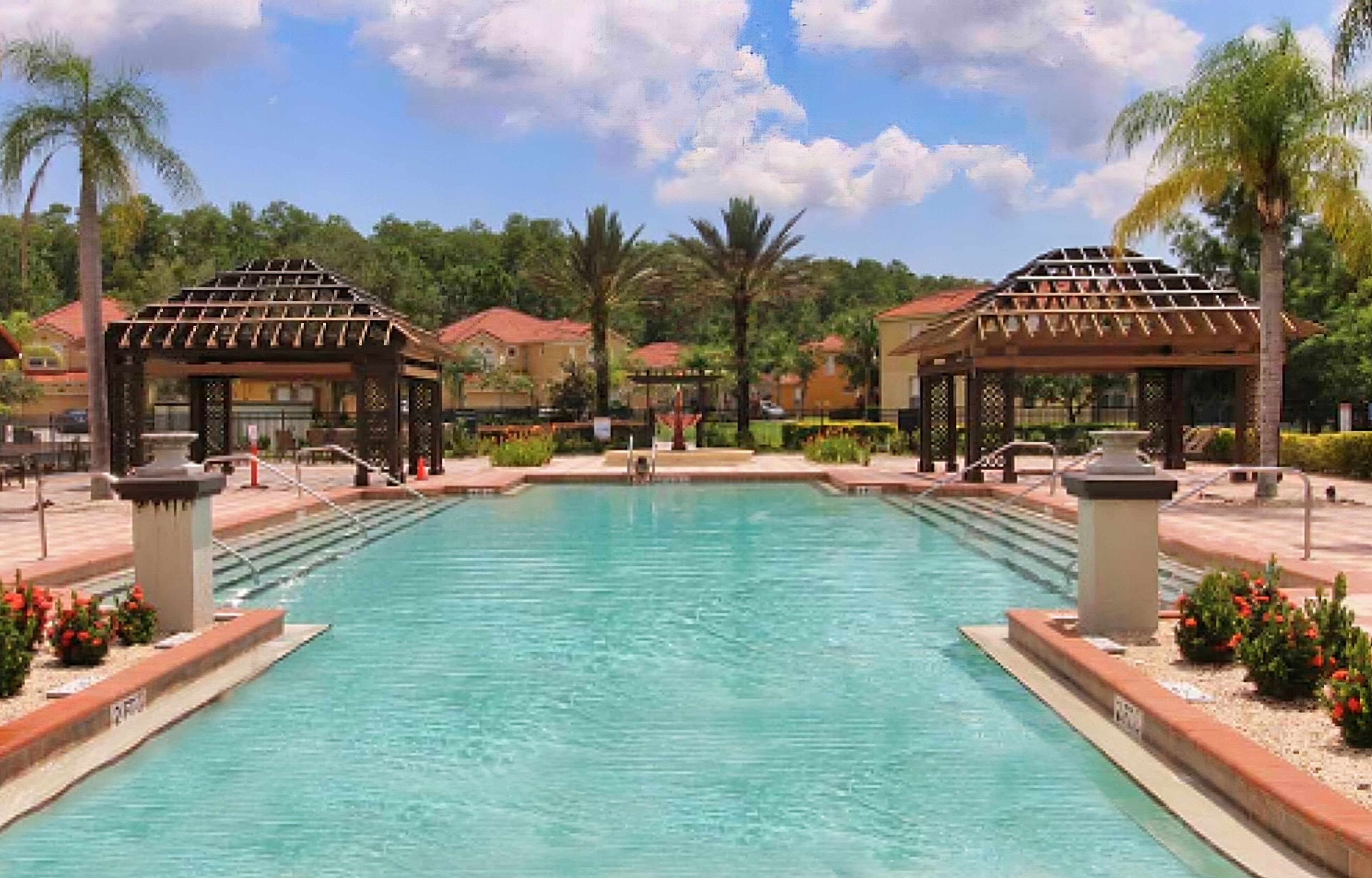 A swimming pool with two gazebos, palm trees, and a clear sky.
