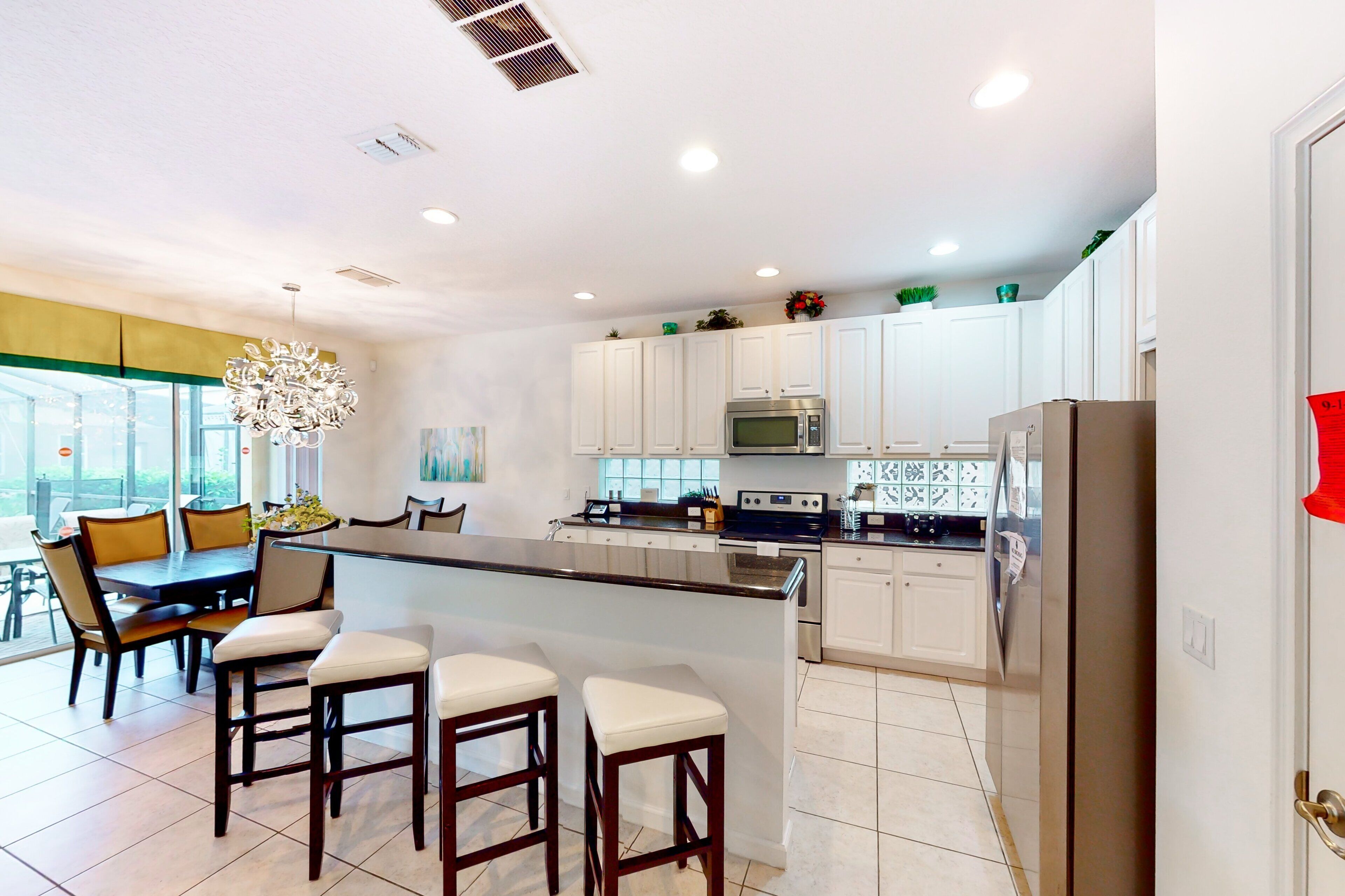 A modern kitchen with white cabinets, a central island with bar stools, a microwave, oven, and refrigerator.