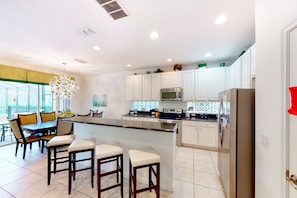 A modern kitchen with white cabinets, a central island with bar stools, a microwave, oven, and refrigerator. - Gated-entry Townhome With Private Pool, Patio, Game Room, AC, & W/D (Davenport)