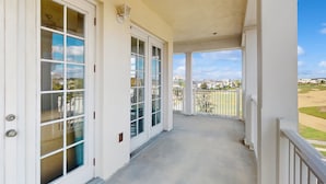Ein überdachter Balkon mit weißen Geländern, einem Betonboden und Blick auf einen Golfplatz.