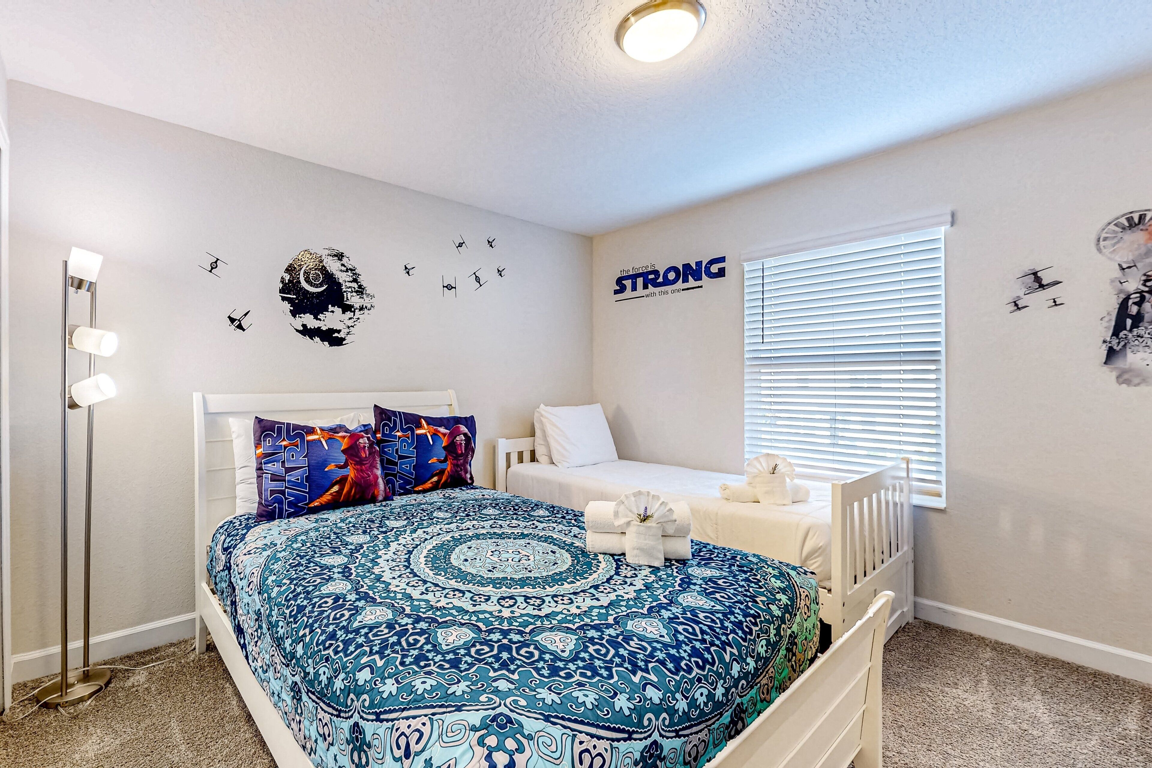 A bedroom with a Star Wars themed bedspread, a bedside table with a lamp, and wall decals including a 'STRONG' motivational quote.