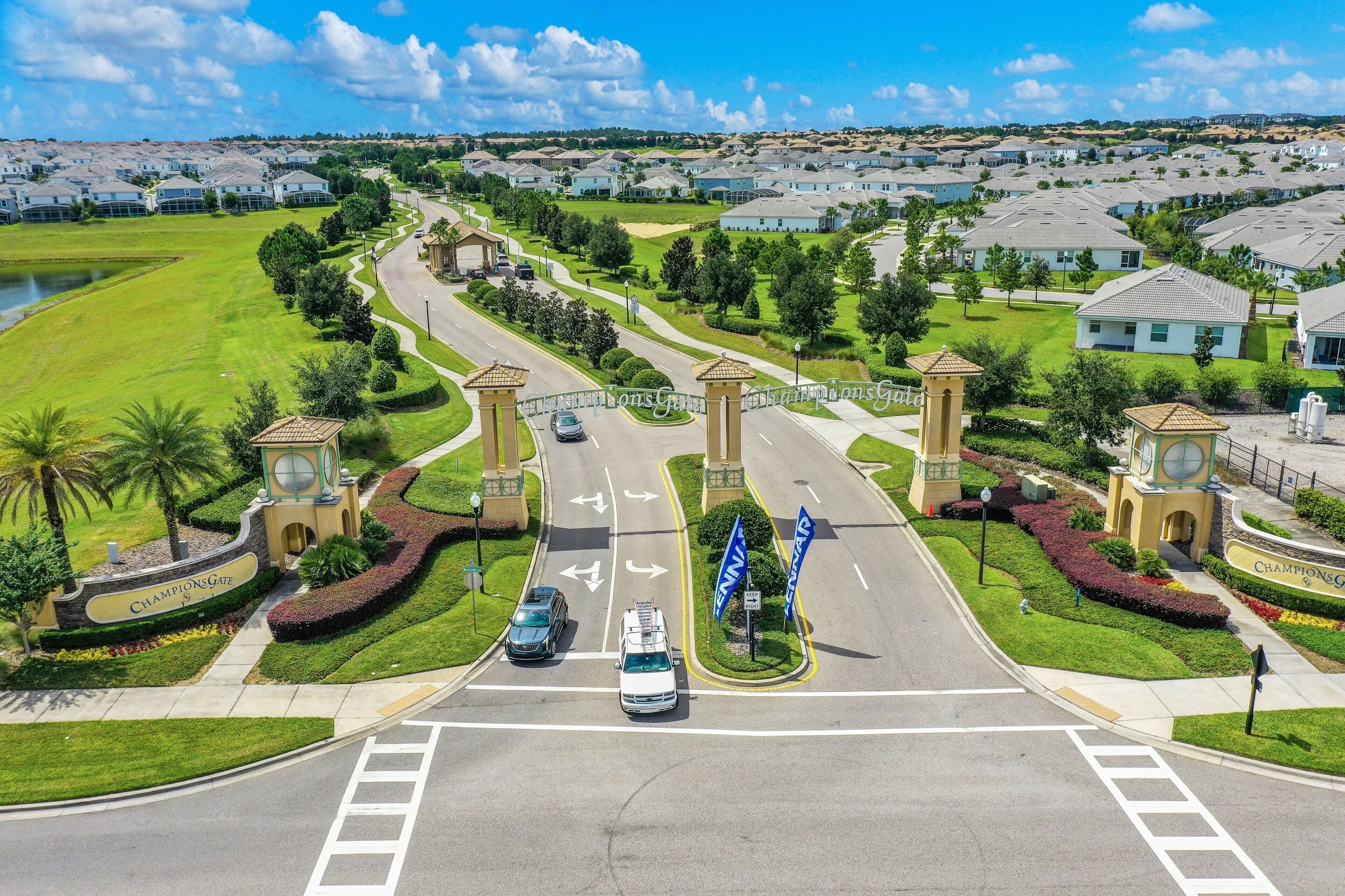 A residential area with a gated entrance, a road with directional arrows, and a clear sky.